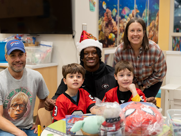 Chris Cole in a Santa hat with a family and two boys in Georgia jerseys at a hospital toy drive